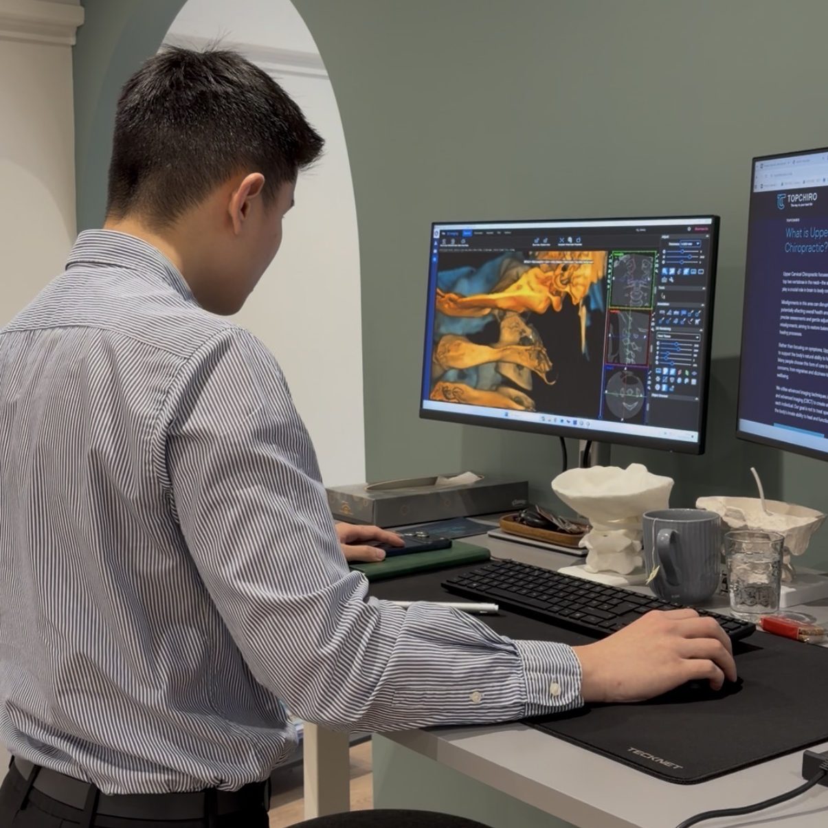 A chiropractor reviewing 3D upper cervical imaging on dual monitors to assess spinal alignment and nervous system health.