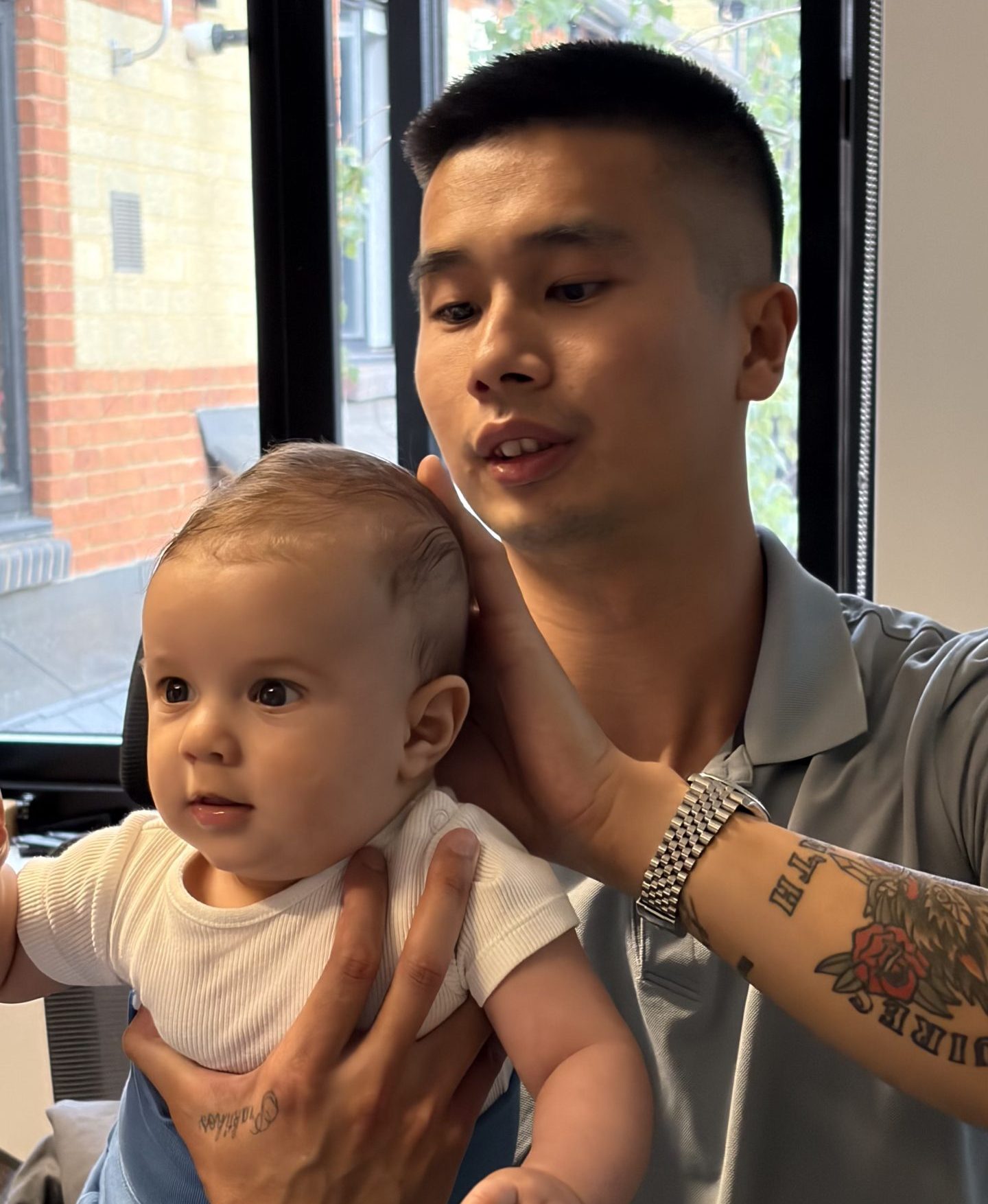 A male chiropractor with a silver watch is conducting a gentle, specific assessment of an infant's neck.
